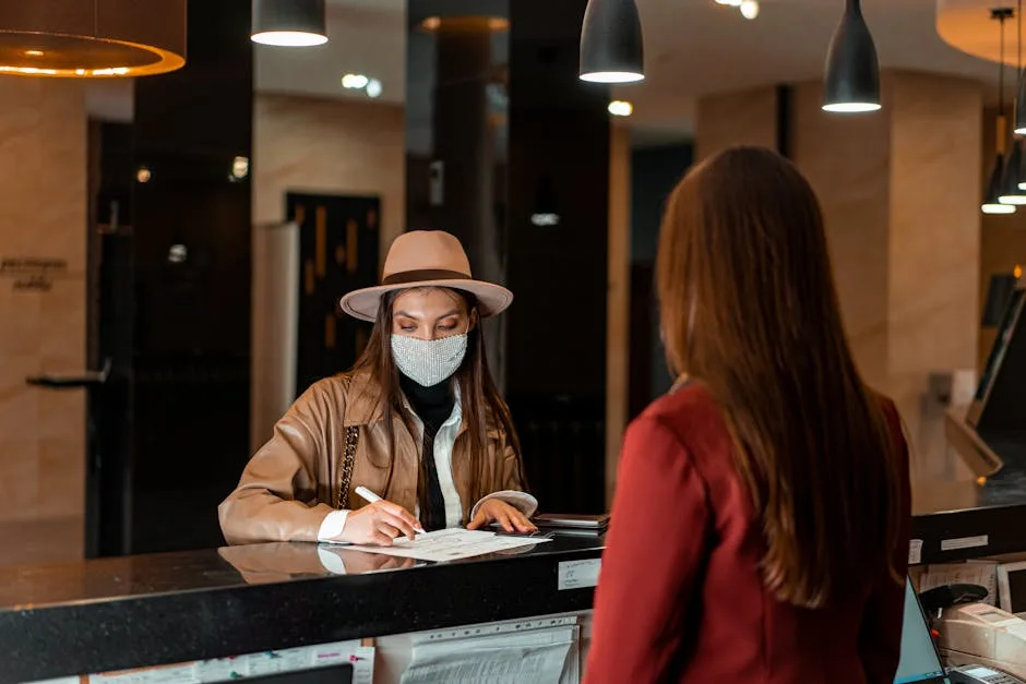 Opret Virksomhed på Amager: CVR og Skatteregler Guide 3 A woman in a hat and face mask checks in at a hotel reception, interacting with a receptionist.
